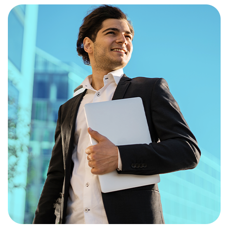 Homem de terno sorrindo ao ar livre enquanto segura um notebook.