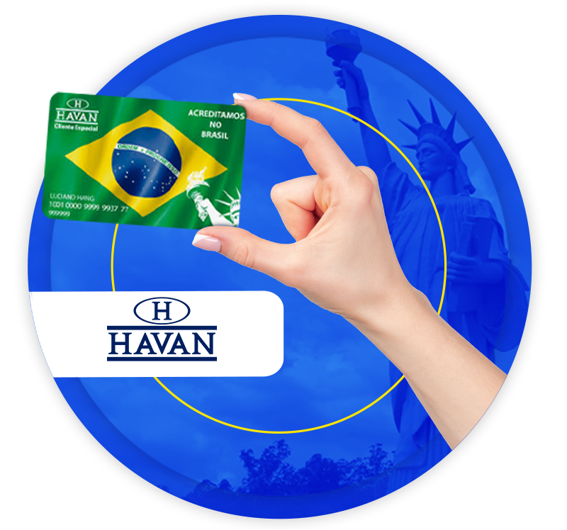 uma mão feminina segurando um cartão da Havan, com a bandeira do Brasil impressa nele, tendo ao fundo a Estátua da Liberdade da Havan