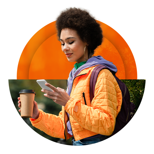 Mulher jovem caminhando na rua com o celular em uma mão e um copo descartável de café na outra