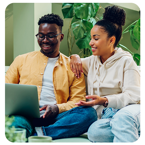 Casal de jovens negros, sentado no sofá de casa, sorrindo , olhando o notebook.