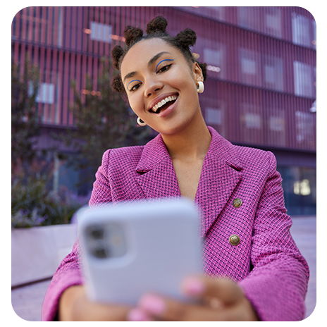Mulher jovem negra, sorrindo, na rua, olhando o celular.