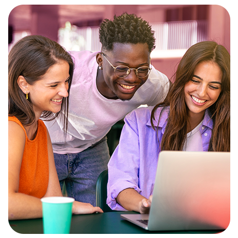 Um jovem negro e duas jovens de cabelo castanho, os três sorrindo e uma mesa de lanchonete, debruçados sobre um notebook.