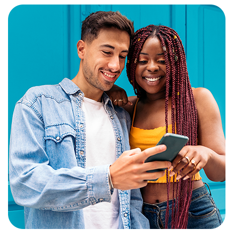 Casal sorrindo olhando celular em frente a fundo azul.