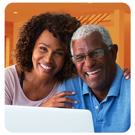 Casal sorrindo em frente ao notebook em ambiente interno.