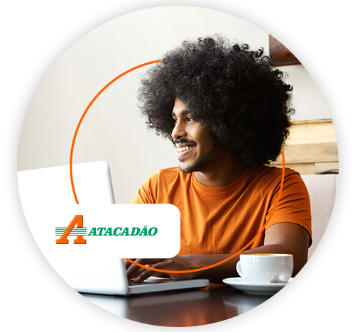 Homem usando notebook em casa, com logo do Atacadão em destaque.